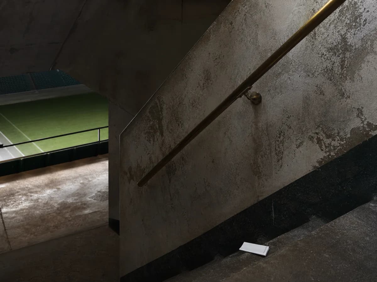 Slitt stadionbetong, messingrekkverk og en umerket papirbillett ved trappen mot banen